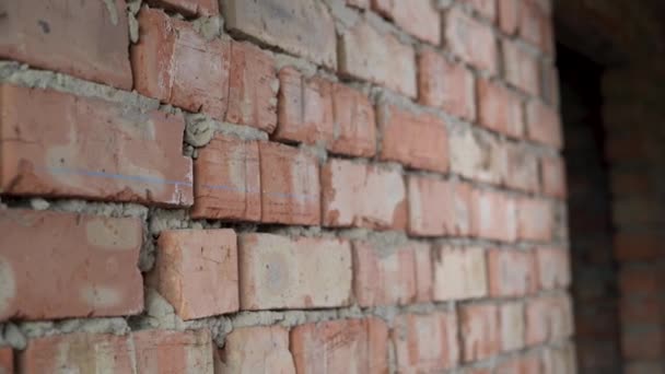 Un trabajador de la construcción masculino está usando un sombrero duro naranja protector y gafas se acerca a una pared de ladrillo, aplica un nivel de espíritu y mide la posición horizontal. — Vídeos de Stock