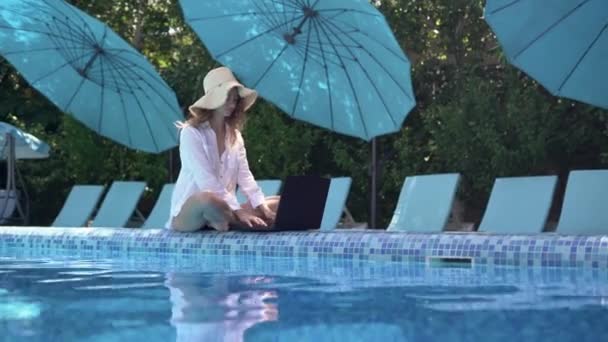 Uma mulher com um portátil na piscina. Trabalho remoto e conceito nômade global. Freelancer jovem no resort t. Teleconferência e trabalho freelance. — Vídeo de Stock