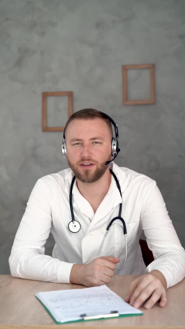 Retrato vertical de amigável sorridente terapeuta profissional adulto sentado no local de trabalho feliz confiante médico masculino sênior vestindo vestido médico telemedicina branca. — Vídeo de Stock