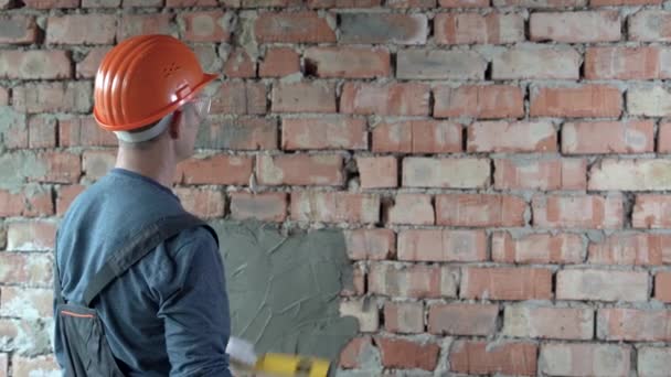 Um construtor masculino caucasiano vestido com um uniforme e um chapéu duro laranja em sua cabeça aplica um nível de espírito para a parede e medir uma linha horizontal reta. — Vídeo de Stock