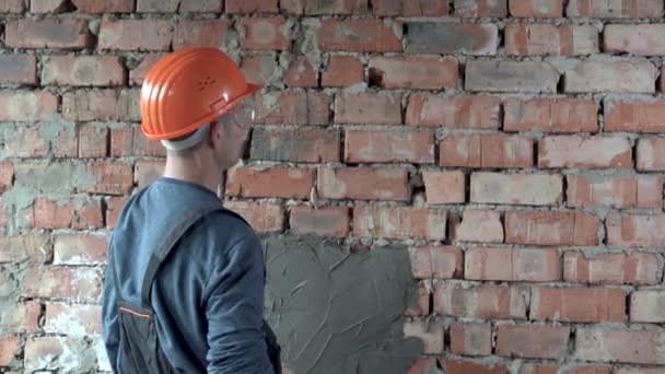 Tuğla duvarın yanında duran bir inşaatçı bir bina sayacını indirir ve ölçümler yapar.. — Stok video