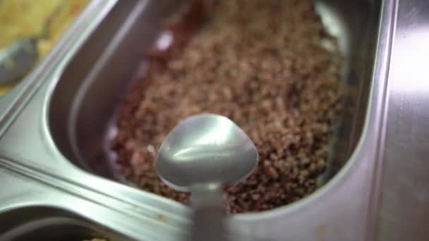 A portion of boiled buckwheat is collected on a large spoon in a buffet on the food distribution line and dinner is put on a plate. First person camera movement. — Stock Video