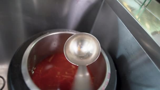 In the buffet, from a large saucepan on the food distribution line, the Ukrainian national dish, red borscht, is collected on a ladle. — Stock Video