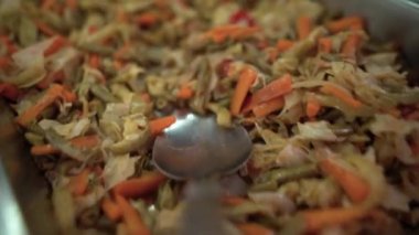 Yemek odasındaki ya da büfedeki büyük kepçenin yakın plan görüntüsü ile sebze güveci alınıp bir tabağa konur..