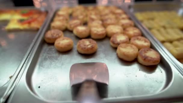 Op een grote lepel in het buffet verzamelen ze verschillende gebakken kazen, een zoet dessert gemaakt van kwark op de voedseldistributielijn. Buffetvoedingsconcept. — Stockvideo