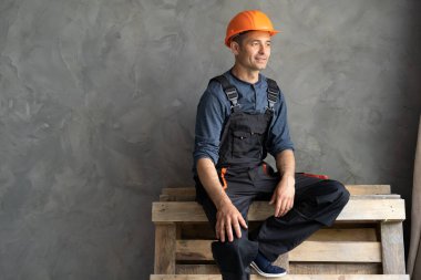 Erkek müteahhit evin içindeki beton duvarın yanında çalışırken dinleniyor. Kapalı alanda işini bitiriyor. Yorgun ustabaşı pencereden dışarı bakıyor. İnşaat ve yenileme konsepti.