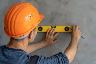 Duvarın sert başlık kontrol seviyesindeki mimar ya da inşaat işçisi. Miğferli bir müteahhit duvarı bir seviyeyle ölçer. Odada bir ustabaşı. yenileme konsepti.