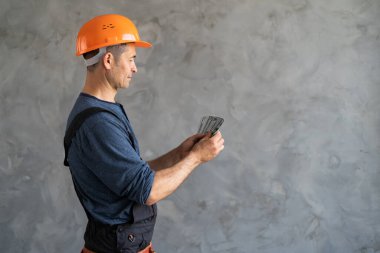 Profildeki erkek ustabaşı para sayıyor iş sözleşmesi için yapılan ödemeler duvarın yanındaki gri arka planda duruyor. Maaş. İş konsepti ve tamir hizmetleri. Metin için yer.