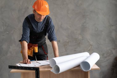 Çalışma masasının yanında bina planları olan bir mimar. Koruyucu kask takan bir mühendisin çizimleri. İnşaat ve bina tasarımı kavramı. Metin için yer.