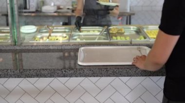 Bir adam açık büfeye ya da yemek odasına gider elinde bir tepsi tutar ve akşam yemeği konsepti olarak kendi yemeğini seçer..