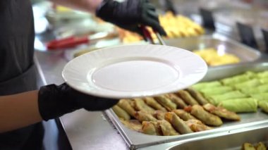 Siyah eldivenli bir garsonun elleri yemek odasındaki ya da açık büfedeki bir tabağa yemek koyar. Etle doldurulmuş peletler.