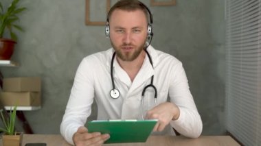 Bir teletıp konsültasyonu sırasında kameraya konuşan beyaz bir doktor sanal bir sohbet toplantısında bir hastaya danışıyor. Uygulama videosu, vesikalık fotoğraf. Web kamerası görünümü.