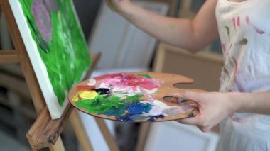 Bir kadın sanatçının eli palette boyaları karıştırıyor ve bir tuval beyaz arka plan stüdyosuna çiçekler çiziyor. Yaratıcılık ve sanat konsepti. Eller sanatsal çiziyor.