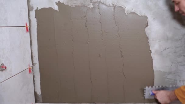 Piastrelle costruttore maschio applica adesivo piastrelle con una spatola o spatola alla parete del bagno. primo piano del lavoro di posa di piastrelle di ceramica. Preparo il muro. concetto di ristrutturazione — Video Stock