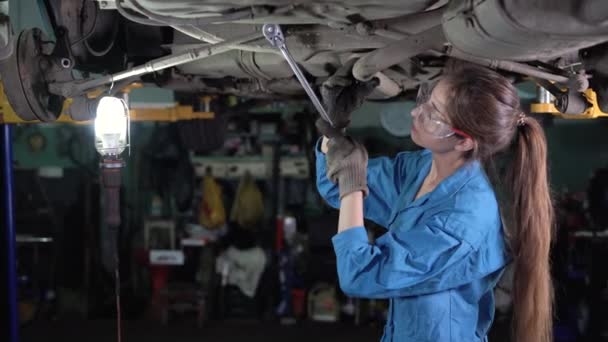 Mechanik samochodowy dziewczyna mechanik w warsztacie stoi w pobliżu samochodu podniesiony w windzie. za pomocą klucza, odkręca nakrętkę. — Wideo stockowe