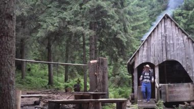 Ormandaki ormancının eski evi, bacadan dumanlar yükseliyor, bastonlu ve sırt çantalı beyaz bir erkek turist kulübeden çıkıp temiz hava soluyor..