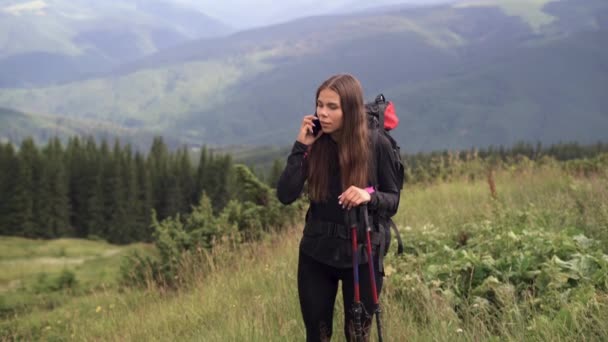 Jonge mooie blanke vrouw wandelaar staat op de top van de berg om te communiceren op haar smartphone met geliefden. — Stockvideo