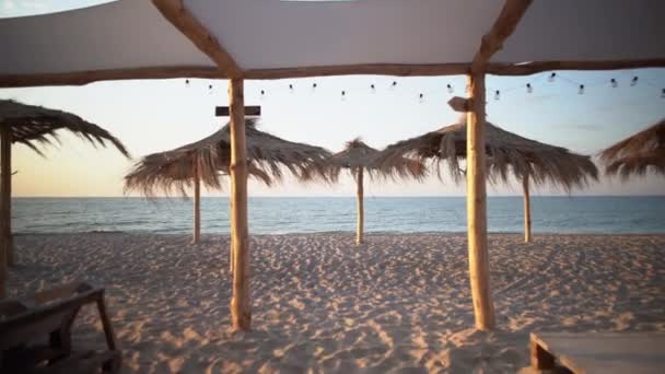 Tropisk strand med halmparasoller på sanden. Tidig morgongryning på havet. En tom semesterort utan folk. — Stockvideo