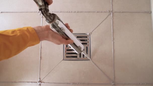 Top view close-up of a man using silicone sealant treats the seams between the tiles in the bathroom. — Stock Video