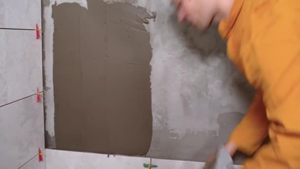 用工具和胶粘剂混合物为瓷砖的铺设准备墙体，进行施工修补。用瓷砖胶粘剂施工时，主建筑商开槽大肠手部的特写. — 图库视频影像