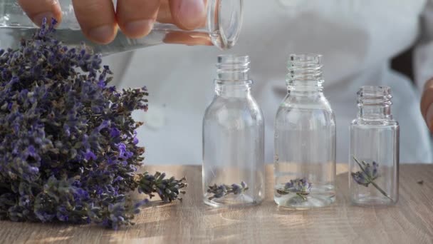 Close-up sobre a mesa são várias garrafas com flores de lavanda, um homem mão derrama álcool nas garrafas. Aromaterapia e produção de perfumes orgânicos naturais. — Vídeo de Stock