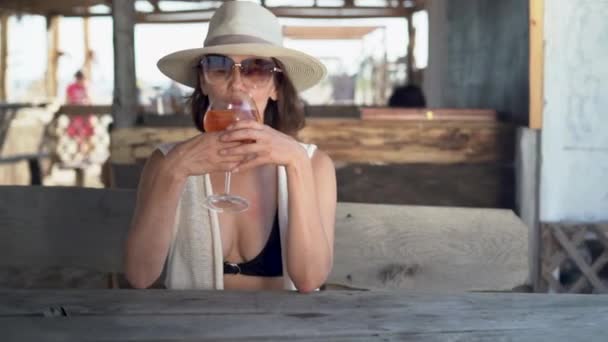 Egy fiatal nő ül egy trópusi üdülőhelyen egy nyári bárban alkoholos koktéllal a kezében, és pihenés közben. — Stock videók
