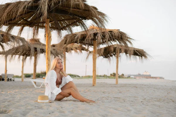 Seksi Beyaz Kadın Kumsalda Saman Şemsiyesinin Altında Tatildeyken Kumsalda Oturur — Stok fotoğraf