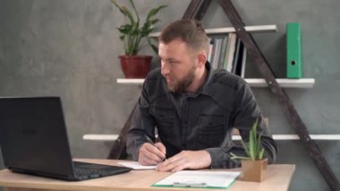 Düşünceli iş adamı online bir proje düşünüyor, işyerindeki bir dizüstü bilgisayara bakıyor, not defterindeki bir kalemle notlar yazıyor, bir öğrenci yeni bir fikir için ilham arıyor