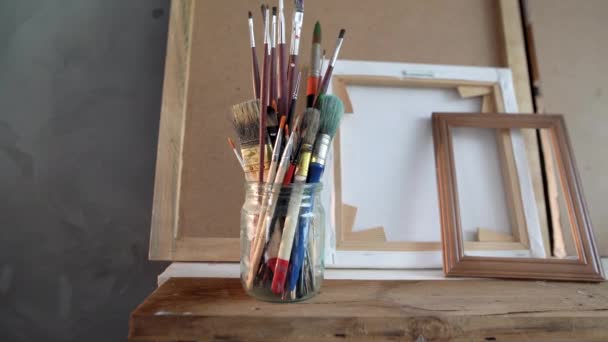 There are paint brushes in a glass jar on a shelf in an art workshop, a mans and a womans hand take them. — Stock Video