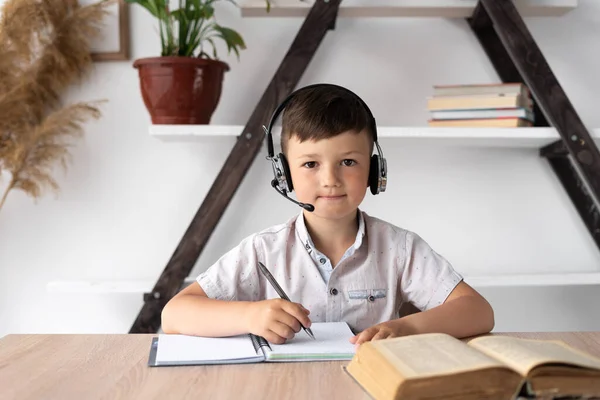 portrait of a schoolboy in headphones listening to a training lesson through a headset. Online education learning a foreign language with a tutor. Remote teacher at home concept.