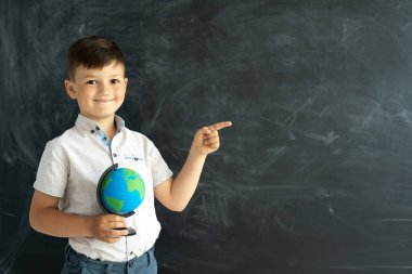 Okulda tebeşir tahtasının önünde duran ve parmağını sağa doğru gösteren bir çocuğun portresi. Eğitim ve öğrenim. Arkaplanda karatahta ve odaklanmış bir öğrenci. metin