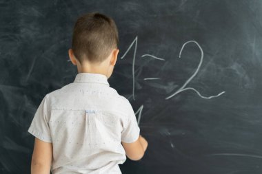 Sınıftaki bir öğrencinin arka planı tahtaya tebeşir numaraları yazar. Matematik dersi. Ortaokul. Eğitim konsepti. Okula dönelim. Mesaj için yer. Boşluğu kopyala