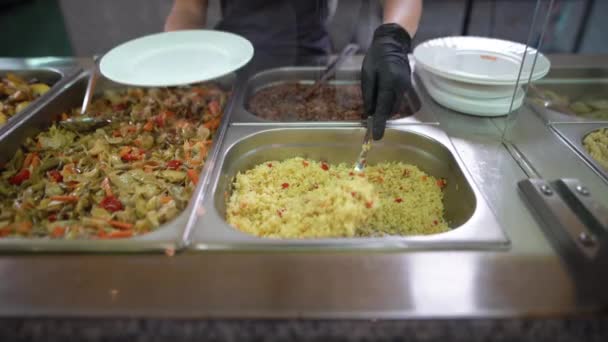 Catering primo piano di una mano di camerieri in guanti di gomma neri dietro un bicchiere posa il riso di cibo in un piatto bianco. protezione contro i virus nei luoghi pubblici. — Video Stock