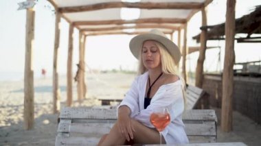 One beautiful woman sits in a bar on the seashore on the table with a glass with a cocktail, she takes her smartphone using the mobile Internet, begins to read the news.