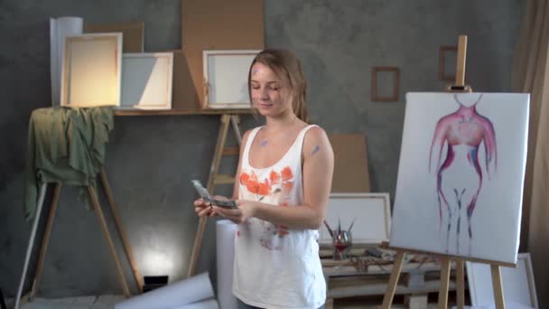 A beautiful Caucasian woman artist stands in an art studio counts money bills of 100 dollars. the concept of earning money on your favorite hobby. — Vídeo de stock