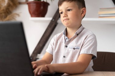 Portrait of a concentrated schoolboy typing on the keyboard of a laptop at home or playing a virtual computer game. motivated boy student studying remotely. wunderkind writes a program for pc.