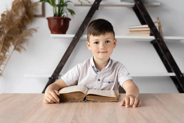 机に座ってオンラインで先生の話を聞いている少年の肖像画です 開いた教科書か本と坐っている宿題をする小学生 家庭教育の概念 高品質の写真 — ストック写真