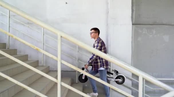 A man with a folded electric scooter is walking up the stairs. Ecological technological lifestyle. Electronic mobility. — Stok video