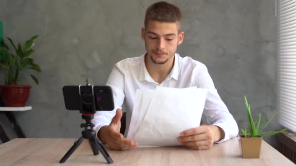 Concentrated caucasian businessman recruiter looking at smartphone screen talking on video communication, arranging meeting with employee reading paper resume sitting at table in home office. — Αρχείο Βίντεο