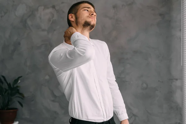 workplace businessman suffering from neck pain while working from office. An overworked young worker massages his neck, feeling muscle pain due to improper posture. Health and lifestyle concept.