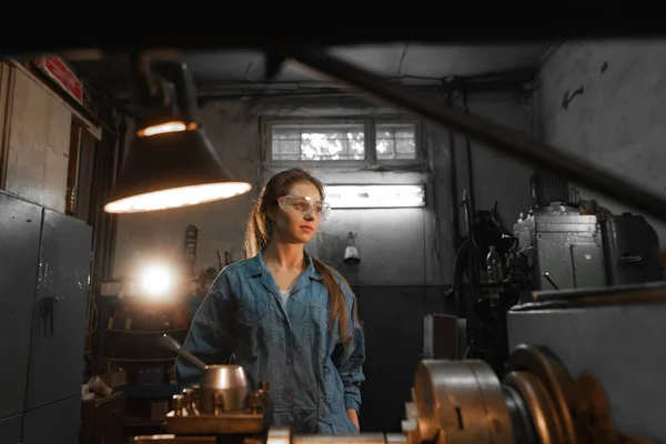 Young woman student works on an automatic lathe CNC, industrial workshop. Concept vocational education turner.