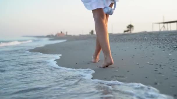 Primer plano de los pies femeninos caminando a lo largo de la arena en la costa al amanecer o al atardecer. — Vídeo de stock