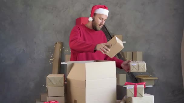 Homem de negócios caucasiano vestindo chapéu vermelho de Papai Noel empilha caixas de artesanato com código de barras. conceito de um monte de vendas e negócios para itens de Natal. — Vídeo de Stock