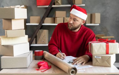 Teslimat şirketinin sahibi Noel 'den önce çalışır ve yeni yıl müşteriye gönderilmeden önce onay için siparişleri kontrol eder. Erkek işadamı teslimat için paket kutusu hazırlıyor. Boşluğu kopyala.