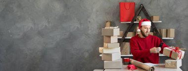Ofiste çalışan, Noel Baba şapkalı bir erkek küçük işletme sahibi müşteriye göndermek için bir kutu malı tarıyor. Noel eşyaları satışı için iş konsepti. Baner. Boşluğu kopyala.