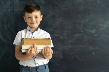 Okula dönelim. Kara tebeşir tahtasının arka planında kitaplarla duran, mesaj için yeri olan öğrenci çocuk. Fakülte öğrencisi zeki çocuk sınıfta. Eğitim ve öğretim kavramı.
