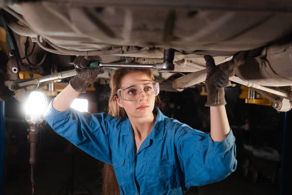 Young beautiful woman car mechanic is dressed in safety glasses and working overalls turns a nut for wrenches. Copy space.