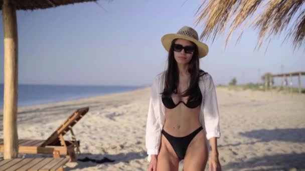 Рано - вранці Кавказька жінка в купальнику і капелюсі ходить уздовж тропічного пляжу на курорті, насолоджуючись сходом сонця і посміхаючись під час відпустки.. — стокове відео