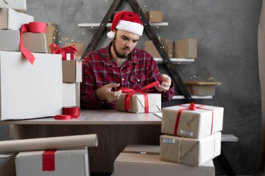 Noel Baba şapkalı bir adam evde çalışır ve çocuklar için Noel hediyesi paketler ve karton bir kutuda ipek kurdeleyle kırmızı bir fiyonk bağlar. Kış tatili için küçük işletme sahibi.