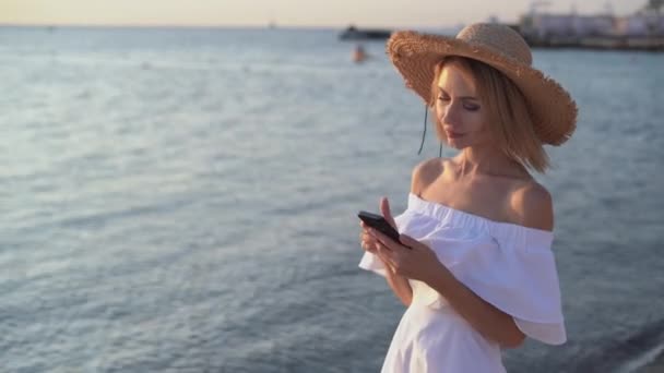 Молода біла жінка йде біля моря або океану рано вранці, тримаючи в руках смартфон, пролітаючи через стрічку новин емоції несподіванки на обличчі . — стокове відео